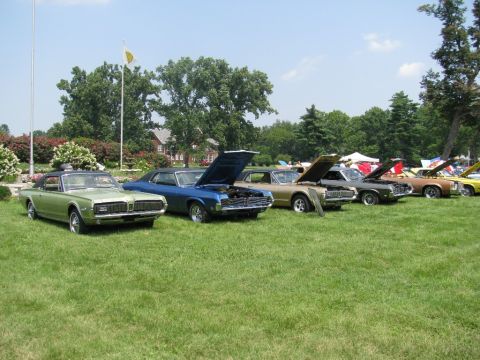 2003 Mercury Marauder - Several classic Mercury Cougar models are displayed on a grassy field under a clear sky.