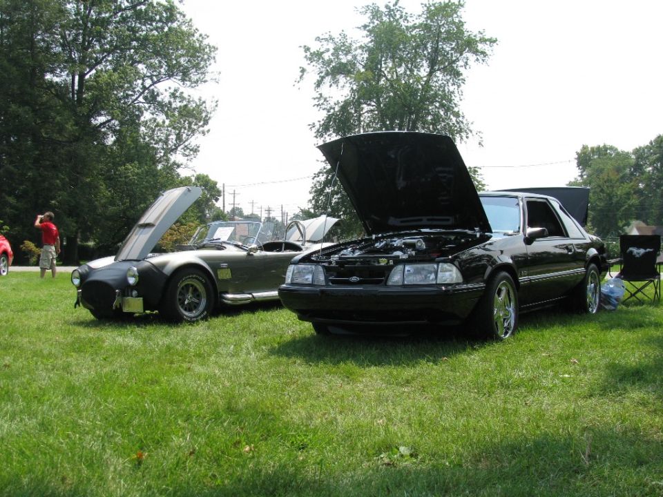 Black Fox-body Ford Mustang LX and AC Cobra roadster at a car show