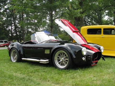 2003 Mercury Marauder - A black AC Cobra with its hood open, red racing stripes and side exhaust pipes, sits on display next to a yellow car.