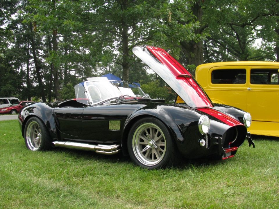 Black AC Cobra with hood open, red racing stripes, side pipes, and chrome wheels