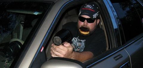 2000 Mercury Grand Marquis - A man sits in the driver's seat of a car, holding a hairdryer and a donut.