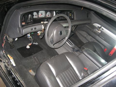 1999 Ford Crown Victoria - Interior of a Mercury sedan shot through the open driver's door, mid-teardown: the dash pad is pulled loose, the instrument cluster and ste…