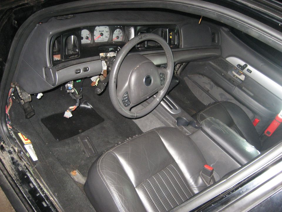 Gray Mercury sedan interior mid-teardown with dash pulled and wiring exposed