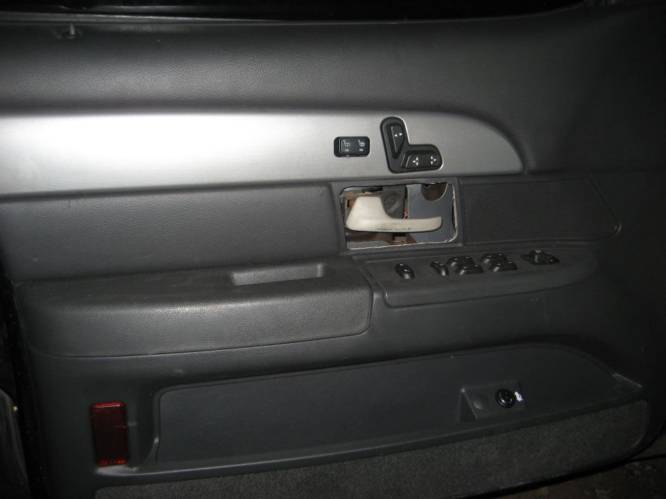 Gray car door panel with handle bezel removed, showing power window and seat switches