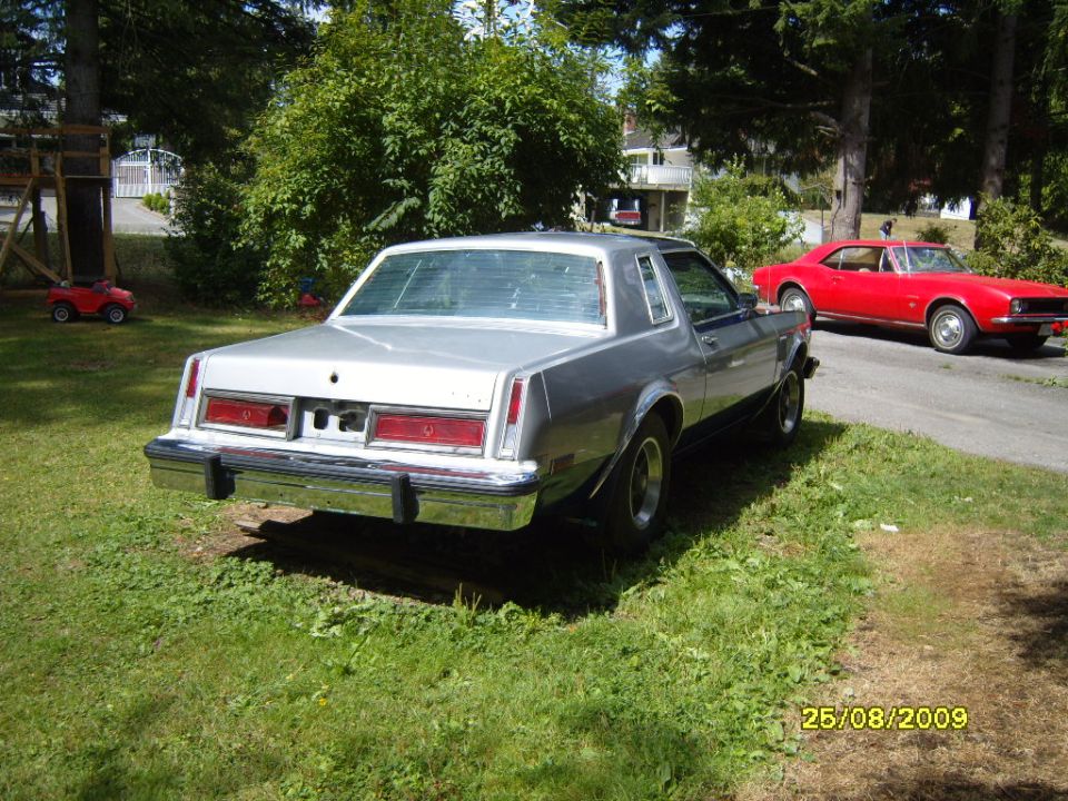 Silver coupe with horizontal blinds on rear window, parked next to a red car. Date stamp shows 25/08/2009