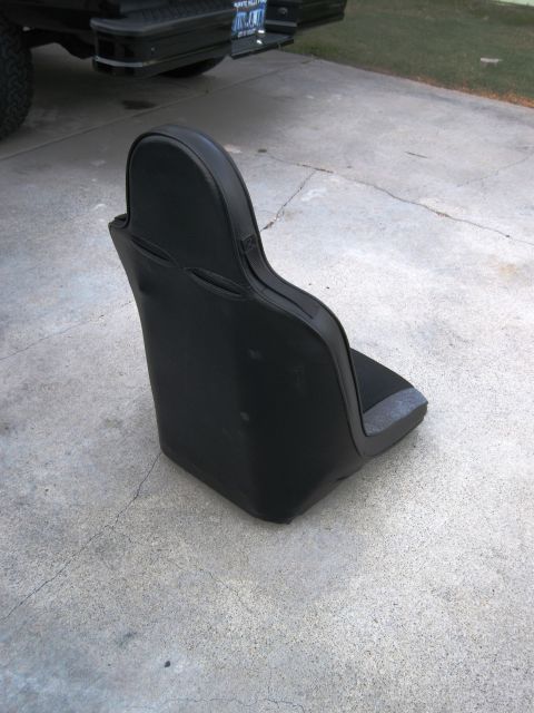 1986 Ford Bronco - A black racing seat sits on a concrete surface with the tailgate of a black truck visible behind it.