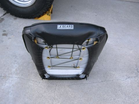 1986 Ford Bronco - A black car seat with a visible brand label is shown from the rear, with a tire and wheel in the background.