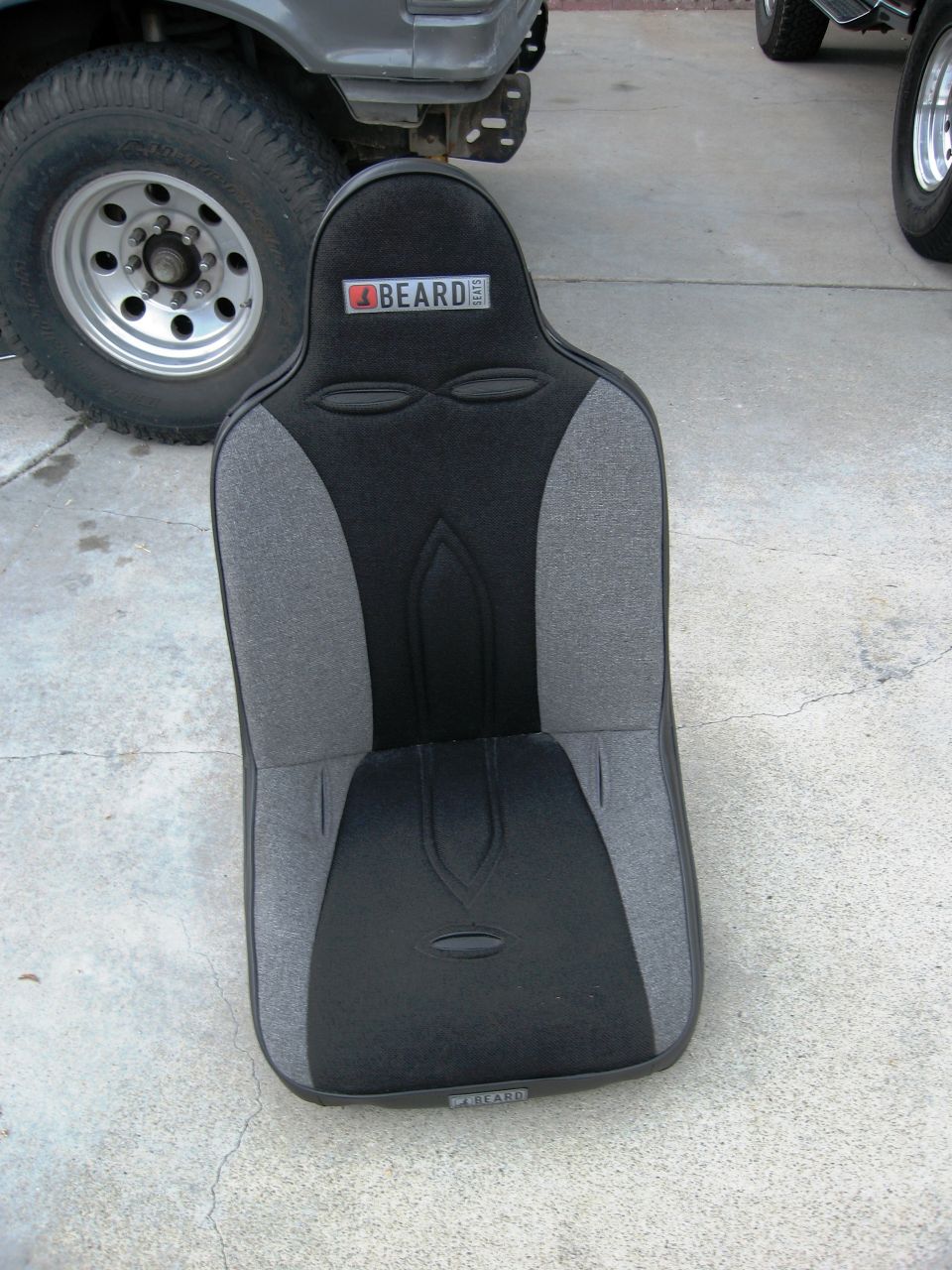 Racing seat with BEARD logo next to a large tire and vehicle fender