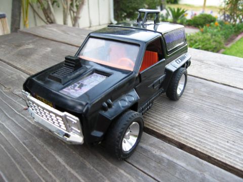 1986 Ford Bronco - A black toy SUV with an orange interior sits on a weathered wooden deck.