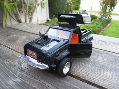 1986 Ford Bronco - This black toy truck features an orange interior and an open driver's side door, sitting on a wooden surface.