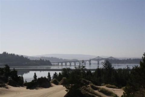1979 Ford Bronco - A wide bridge spans a body of water, with sand dunes and evergreen trees framing the distant landscape under a hazy sky.