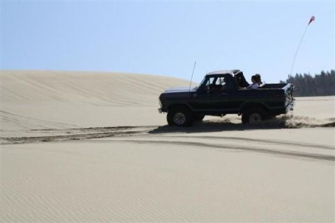 1979 Ford Bronco - Ford Bronco kicks up sand while driving on a dune under a clear blue sky.
