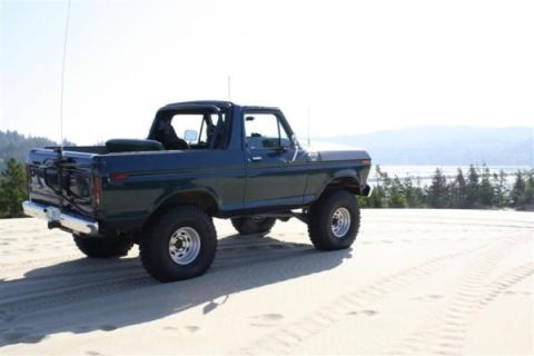 1979 Ford Bronco - A dark green 1978 Ford Bronco sits on sand dunes with a body of water and trees in the background.
