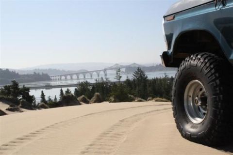 1979 Ford Bronco - A blue 1979 Ford Bronco is parked on a sand dune, overlooking a bridge and bay.