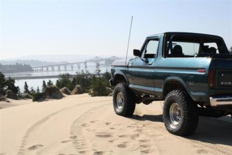 1979 Ford Bronco - Ford Bronco parked on sand dunes with a large bridge and water in the background.