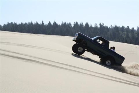 1979 Ford Bronco - Pickup truck navigates a steep sand dune, sending sand flying.