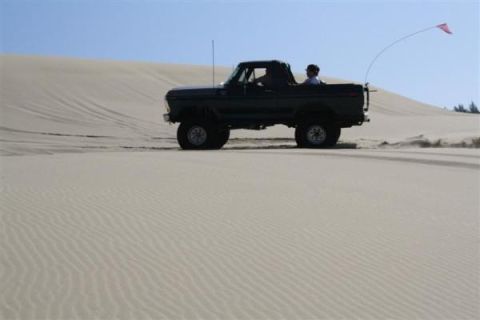 1979 Ford Bronco - A Ford Bronco navigates sandy terrain under a clear blue sky.