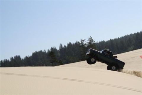 1979 Ford Bronco - A dark pickup truck jumps over a sand dune, kicking up dust.