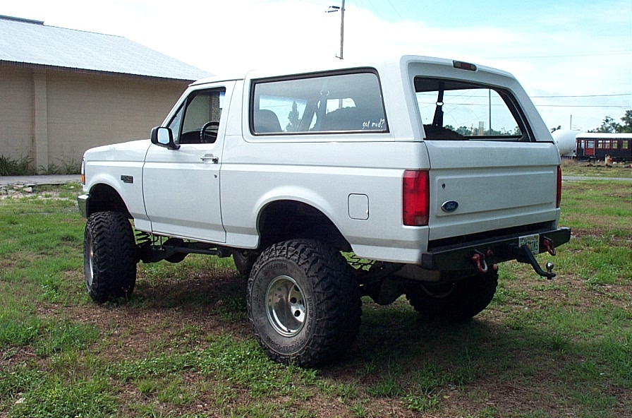 White lifted two-door Ford Bronco SUV on large off-road tires, rear 3/4 view on grass
