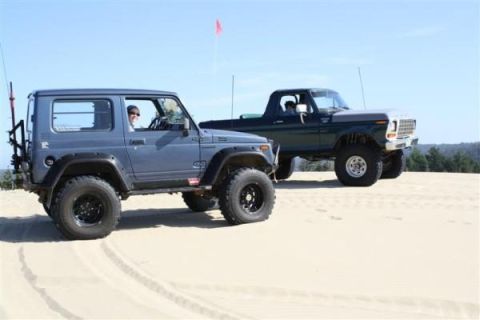 1979 Ford Bronco - Two modified off-road vehicles, a Suzuki Samurai and a Ford Bronco, are parked on sand dunes under a clear sky.