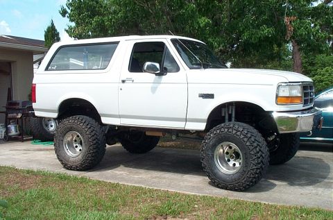 1995 Ford Bronco - A white Ford Bronco with a lifted suspension and aggressive off-road tires is shown from a three-quarter front angle.