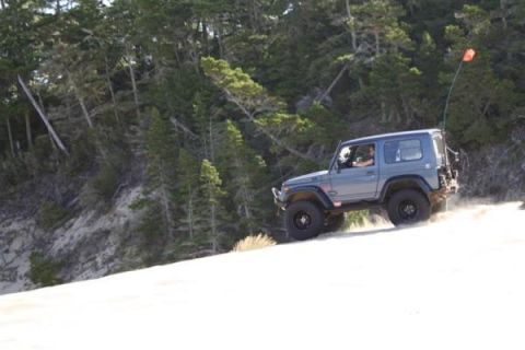 1979 Ford Bronco - An off-road SUV navigates a sandy terrain, kicking up dust as it drives along the dune.