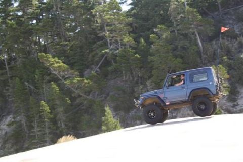 1979 Ford Bronco - Off-road SUV navigates a sandy incline with a wooded hillside in the background.