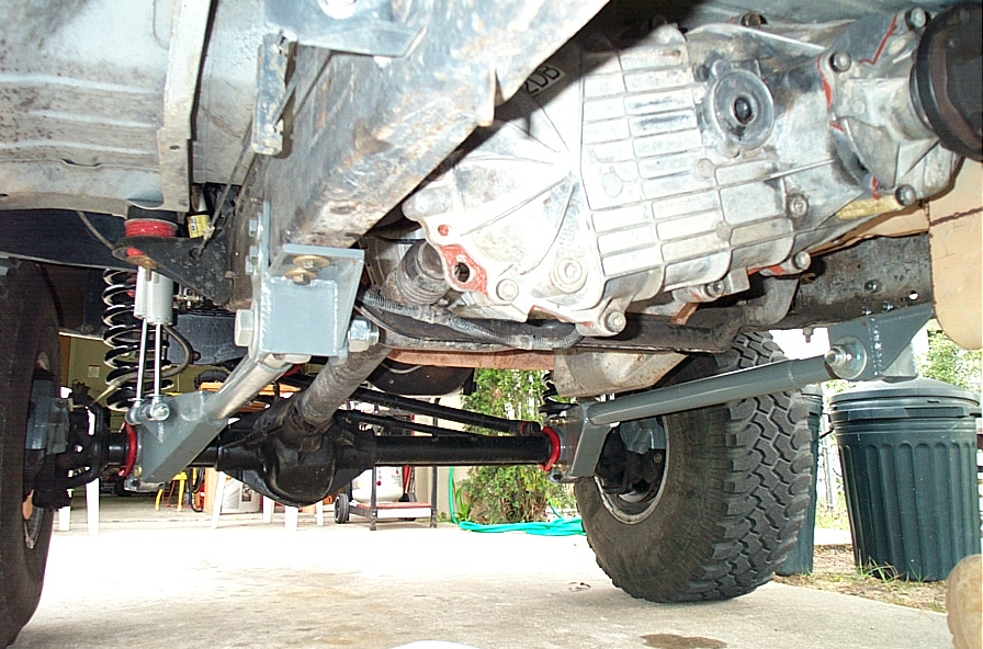 Undercarriage of lifted 4x4 showing transfer case, front axle, coil spring and mud tire