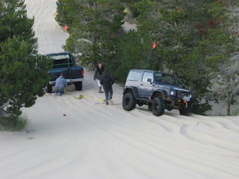 1979 Ford Bronco - Two off-road vehicles are on sand dunes, with people assisting one of them.