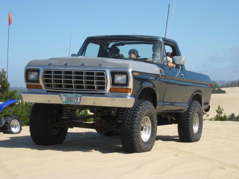 1979 Ford Bronco - This lifted Ford Bronco is parked on a sandy terrain under a clear blue sky.