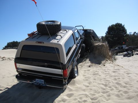 1996 Ford Bronco - This 1996 Ford Bronco navigates sandy terrain, equipped with a roof-mounted spare tire and a flag for visibility.
