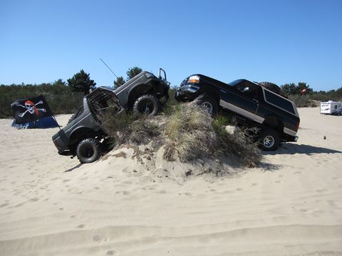 1996 Ford Bronco - Two off-road vehicles navigate a sandy incline under a clear blue sky, with a pirate flag nearby.