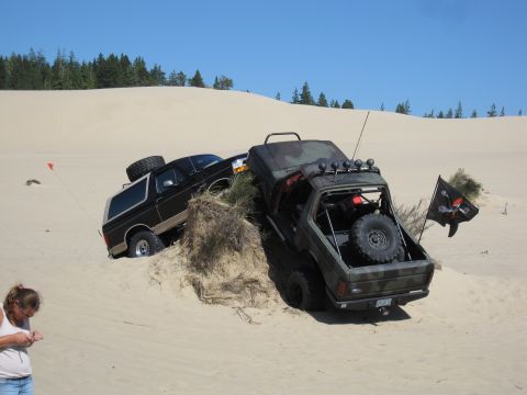 1996 Ford Bronco - Two off-road vehicles navigate sandy dunes under a clear blue sky.