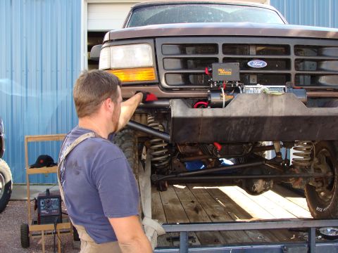 1993 Ford Bronco - A man is working on the front of a Ford truck that has a winch mounted on its custom bumper.