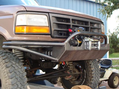 1993 Ford Bronco - The front end of a modified Ford truck, a winch mounted on a custom bumper, with a lawnmower in the background.