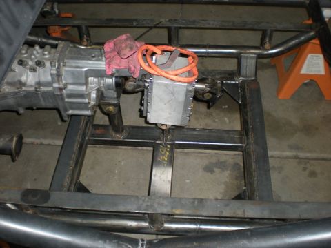 Suzuki Samurai - Bare tube-and-box-section buggy frame on a shop floor, fitted with an aluminum-case manual transmission mated to a boxy aluminum transfer c…