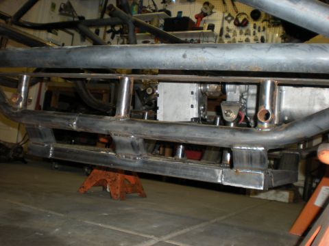 Suzuki Samurai - Side profile of a bare tube-chassis frame on an orange jack stand in a home shop, showing freshly welded rocker tubing, sliders and a flat…