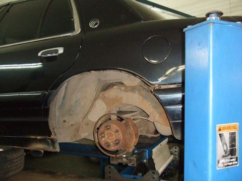 2001 Ford F-150 - The rear wheel well of a sedan is shown while on a lift, revealing the brake drum and suspension components.