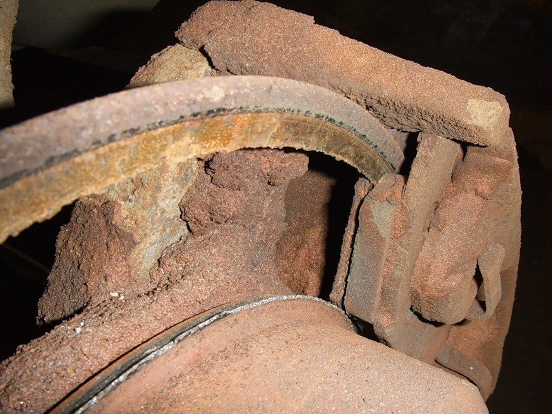 Heavily rusted brake rotor and caliper assembly, showing significant wear and corrosion