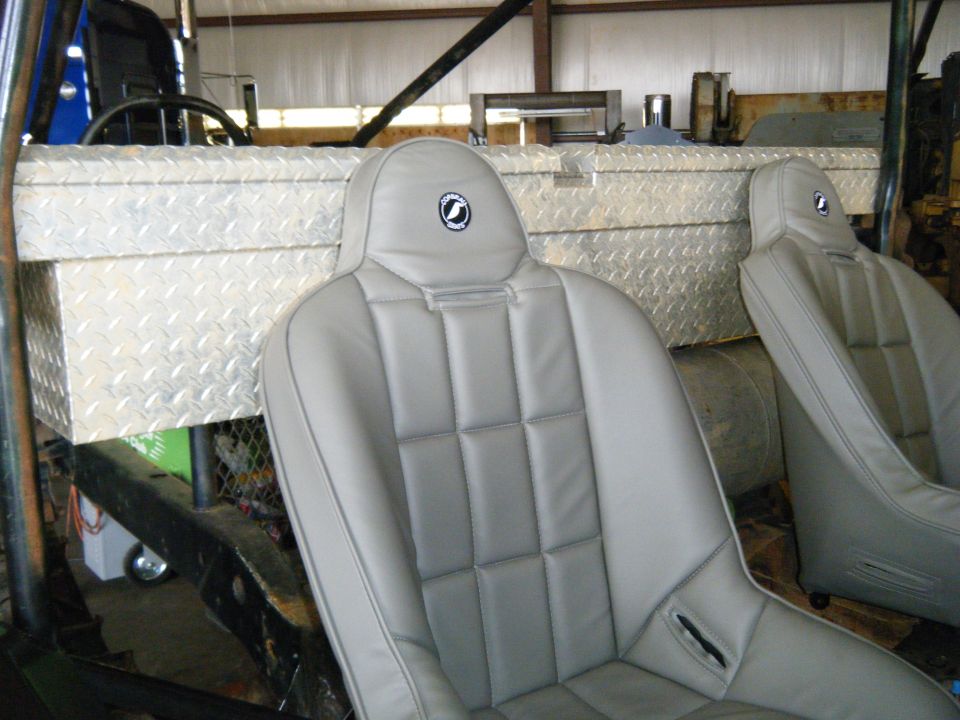 Interior view of a vehicle with two grey racing seats and a diamond plate toolbox mounted behind them