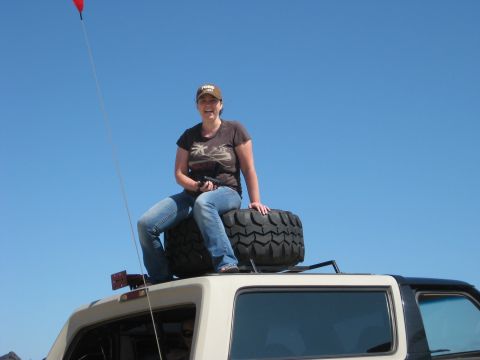 1979 Ford Bronco - A woman sits on a spare tire mounted on the roof of a 1979 Ford Bronco under a clear blue sky.