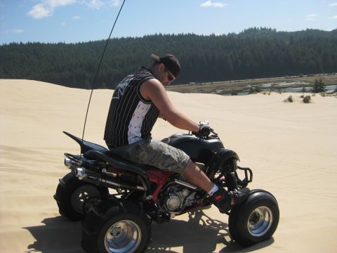 1979 Ford Bronco - Rider on a quad bike navigates sandy terrain with a forested hillside behind.