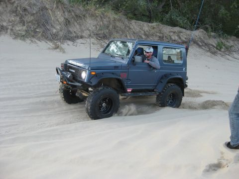 1979 Ford Bronco - A Suzuki Samurai navigates sandy terrain, kicking up dust as it drives.
