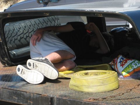 1979 Ford Bronco - A person rests inside the bed of a vehicle, surrounded by gear including a spare tire and a tow strap.