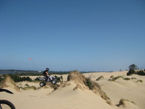 1979 Ford Bronco - A person on an ATV jumps over a sand dune on a clear day.