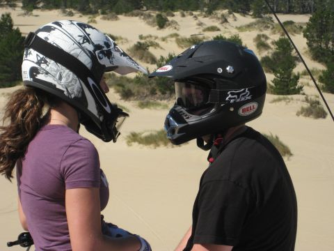 1979 Ford Bronco - Two individuals wearing protective helmets are positioned on a sand dune, facing one another.