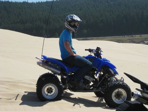 1979 Ford Bronco - Rider on a blue ATV navigates sandy terrain with a forest in the background.