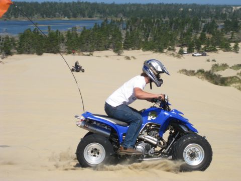 1979 Ford Bronco - Side view of a rider in a white shirt and black-and-white helmet powering a blue sport quad across coastal sand dunes, kicking up sand from…
