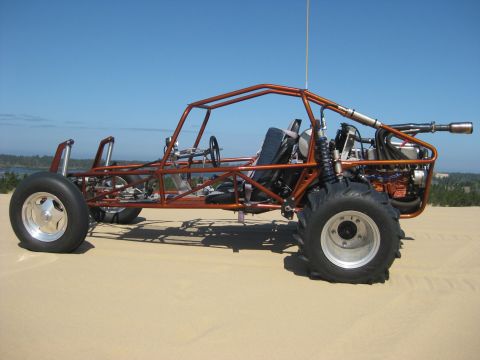 1979 Ford Bronco - A side-view of an orange tube-frame sand rail buggy parked on sand dunes under a clear blue sky, with a mid-mounted engine, exposed roll ca…