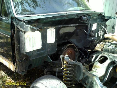 1992 Ford Bronco - The front end of a green vehicle is disassembled, revealing the engine bay and suspension components.